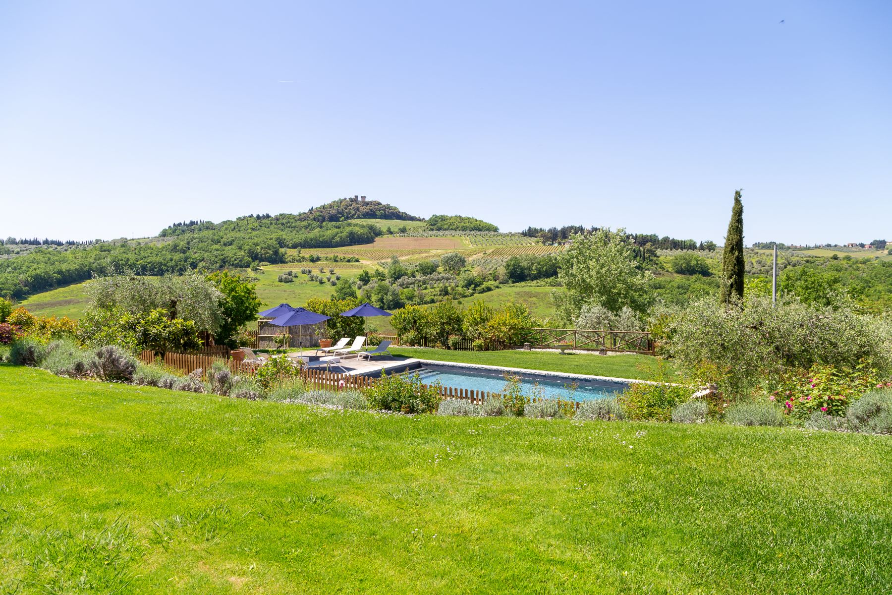 View of the outdoor pool at Villa San Casciano in Tuscany from the garden surrounded by fields and trees
