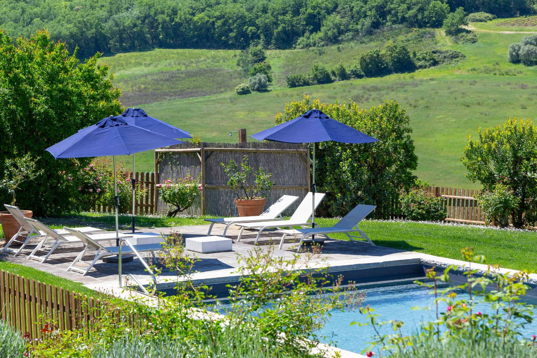 View of the sun loungers and blue umbrellas at the outdoor pool at Villa San Casciano in Tuscany
