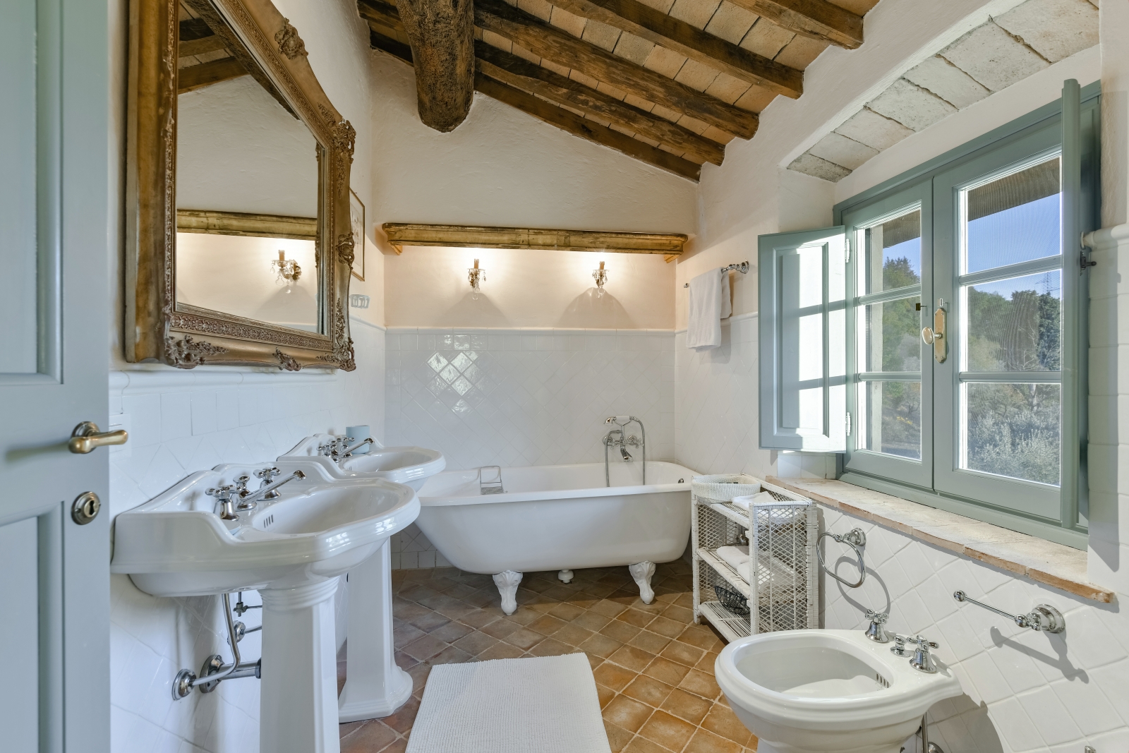 Bathroom with sinks, bidet, shelves, bathtub, large mirror and window at Villa San Casciano in Tuscany, Italy