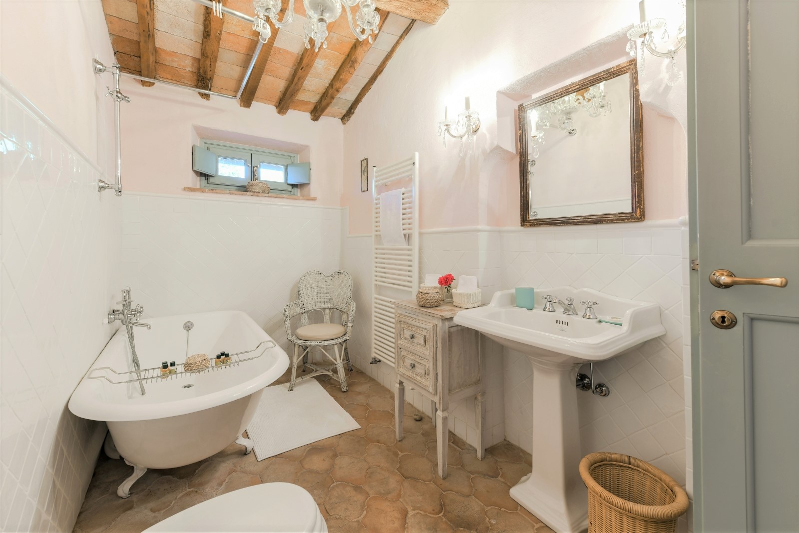 Bathroom with bath, chair, towel rail, cabinet, sink, chandeliers and mirror at Villa San Casciano in Tuscany, Italy