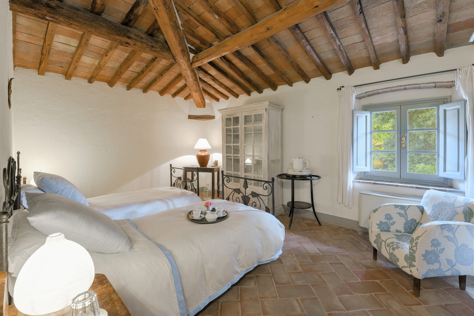 Bedroom with twin beds, lamp, armchair, tables, cabinet and window at Villa San Casciano in Tuscany, Italy