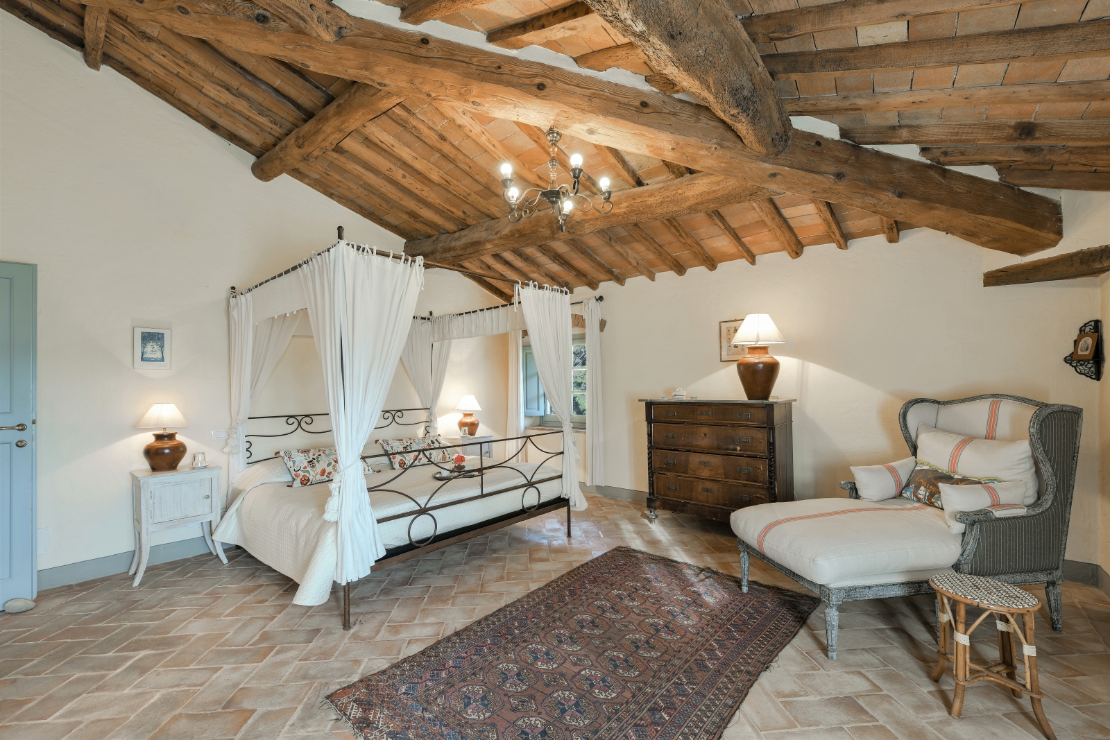 Bedroom with four poster double bed, tables, lamps, chaise longue and drawers at Villa San Casciano in Tuscany, Italy
