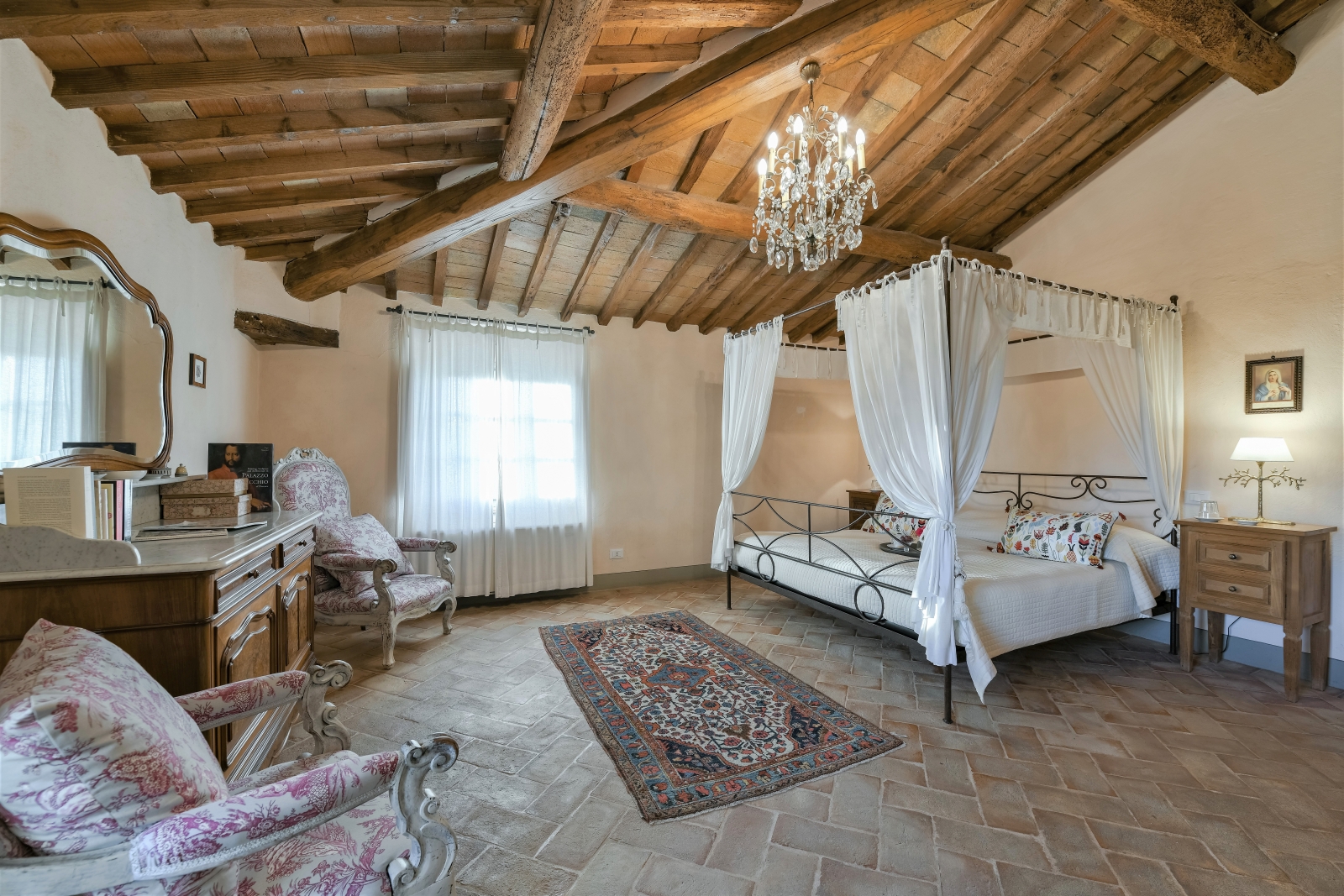 Bedroom with four poster double bed, table, armchairs, cabinet, mirror and chandelier at Villa San Casciano in Tuscany, Italy