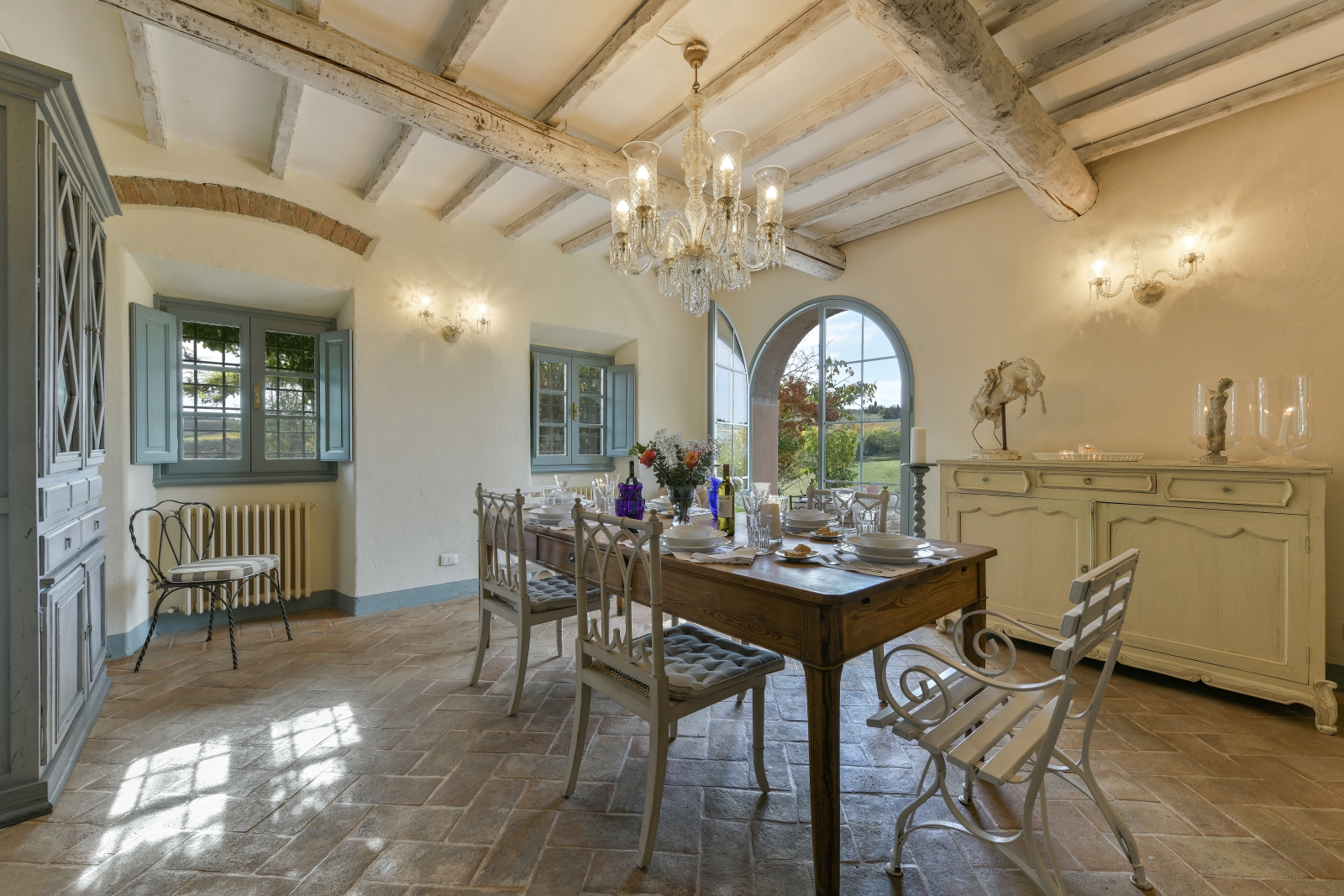 Dining room with table, chairs, crockery, cabinets, chandelier and French doors at Villa San Casciano in Tuscany, Italy