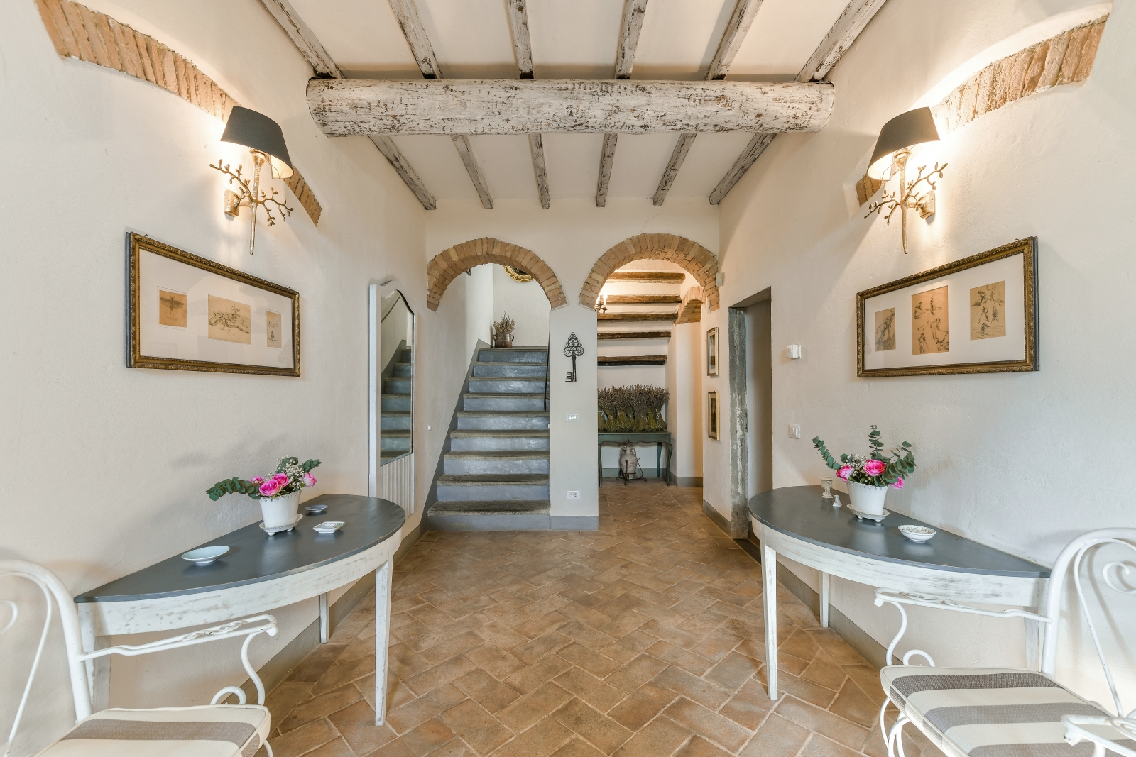 Hallway with console tables, chairs, lights, picture frames and stairs at Villa San Casciano in Tuscany, Italy