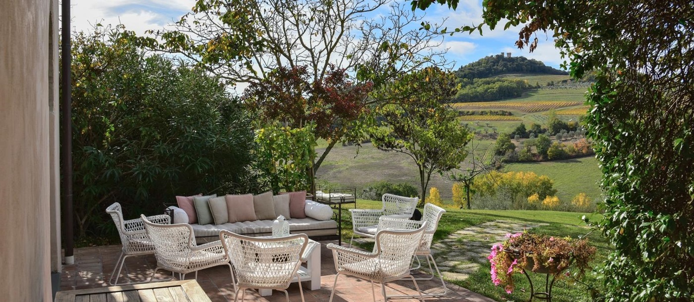 Outdoor seating area with chairs, sofa, table and view of garden and countryside at Villa San Casciano in Tuscany, Italy