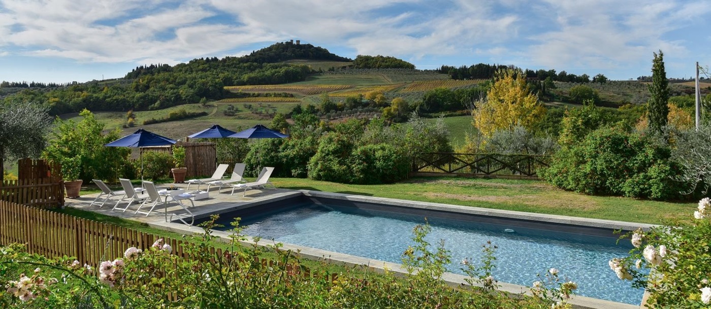 Pool and patio with sun loungers, umbrellas, tables and view of countryside at Villa San Casciano in Tuscany, Italy