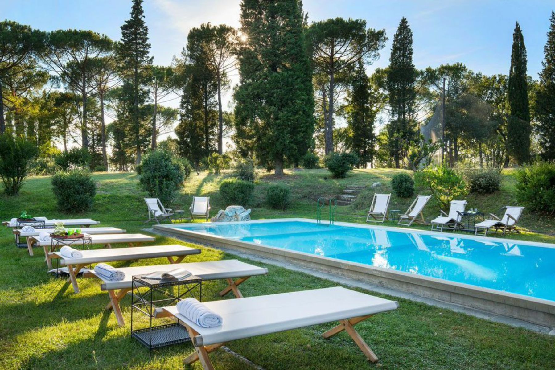 View of the outdoor pool surrounded by trees featuring white sun loungers around the pool on grass
