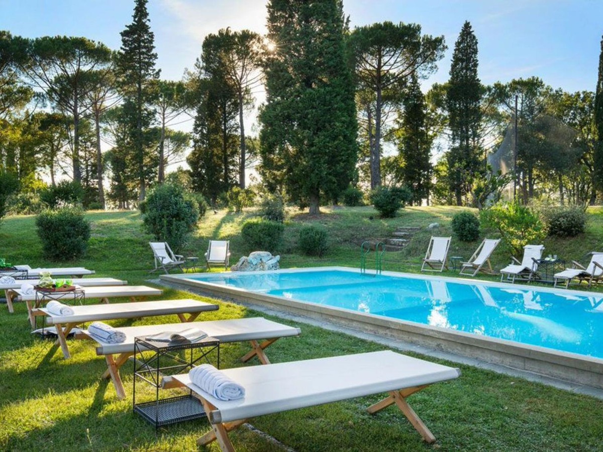 View of the outdoor pool surrounded by trees featuring white sun loungers around the pool on grass