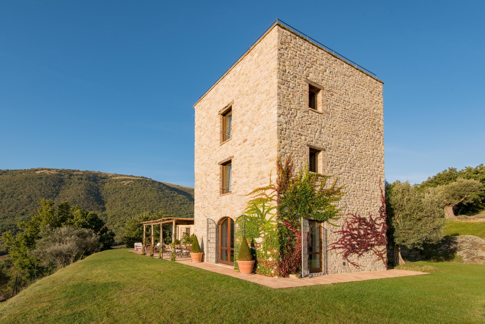 Garden and back of villa with patio, ivy, plants, trees and mountains at Bel Canto in Umbria, Italy