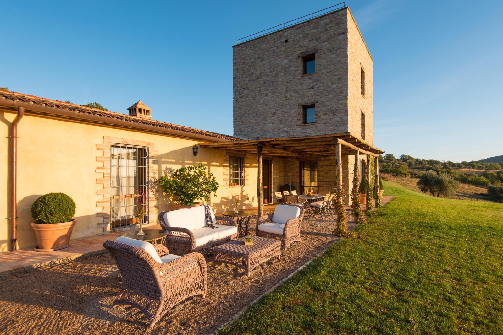 Patio with comfy chairs, coffee table, covered dining area, long table, plants and grass Bel Canto in Umbria, Italy