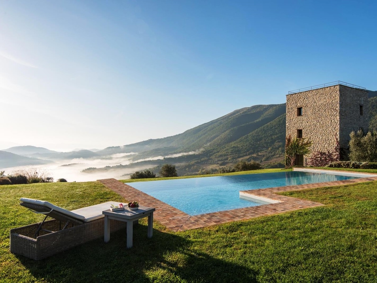 Pool with sun lounger, coffee table, fruit, green grass and view of mountains and villa at Bel Canto in Umbria, Italy