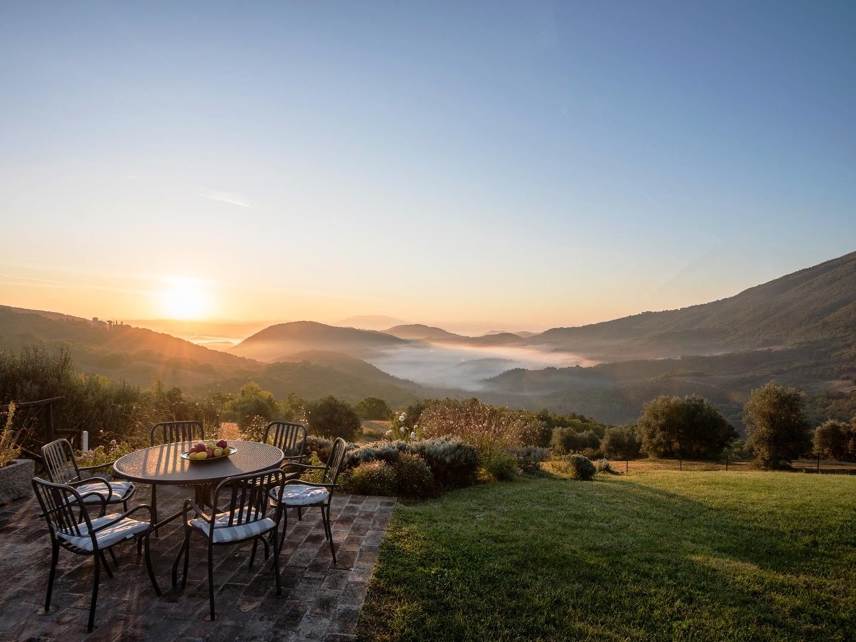 Patio with table, chairs, fresh fruit, grass, plants, trees and view of mountains and sunset at Bel Canto in Umbria, Italy