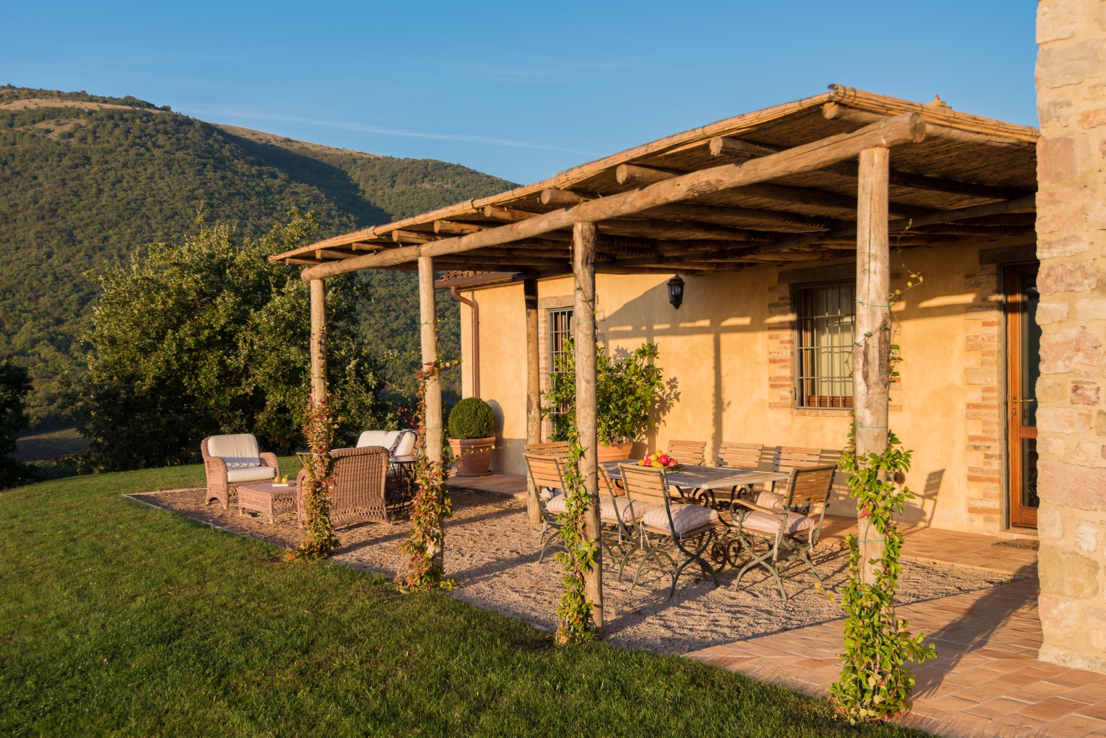 Patio with covered dining area, table, chairs, fruit, plants, comfy chairs and mountain view at Bel Canto in Umbria, Italy