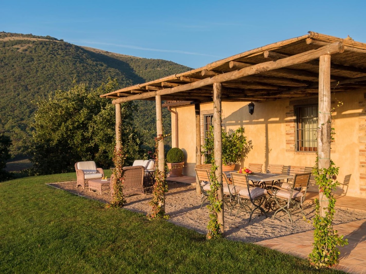 Patio with covered dining area, table, chairs, fruit, plants, comfy chairs and mountain view at Bel Canto in Umbria, Italy