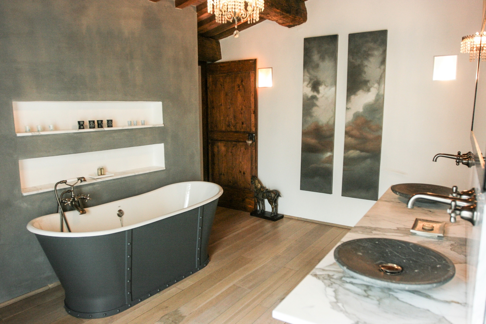 Bathroom with bath, shelves, chandelier, marble sinks, mirror and horse door stop at La Spiga in Umbria, Italy