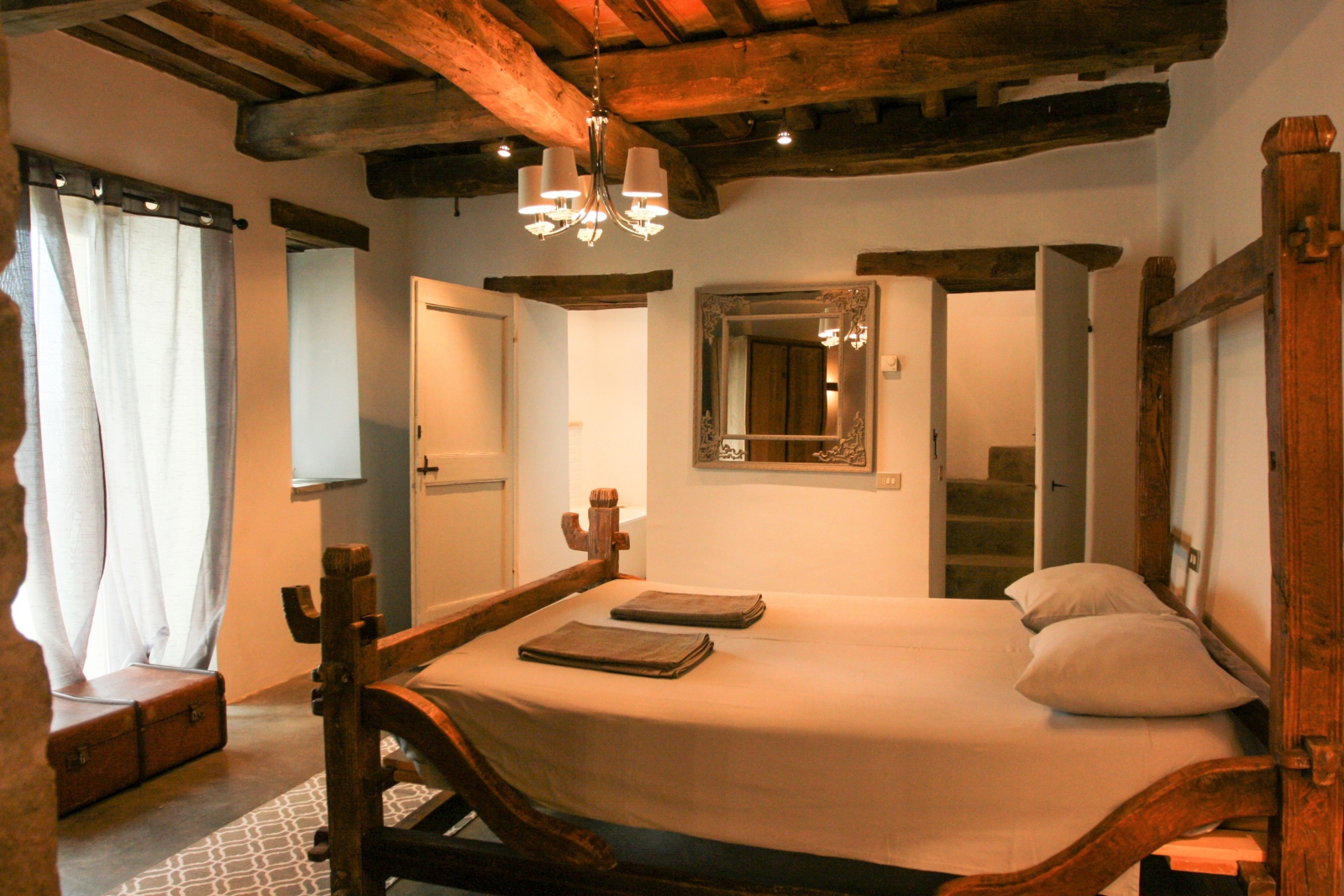 Bedroom with double bed, large window, hanging light, mirror and ceiling beams at La Spiga in Umbria, Italy