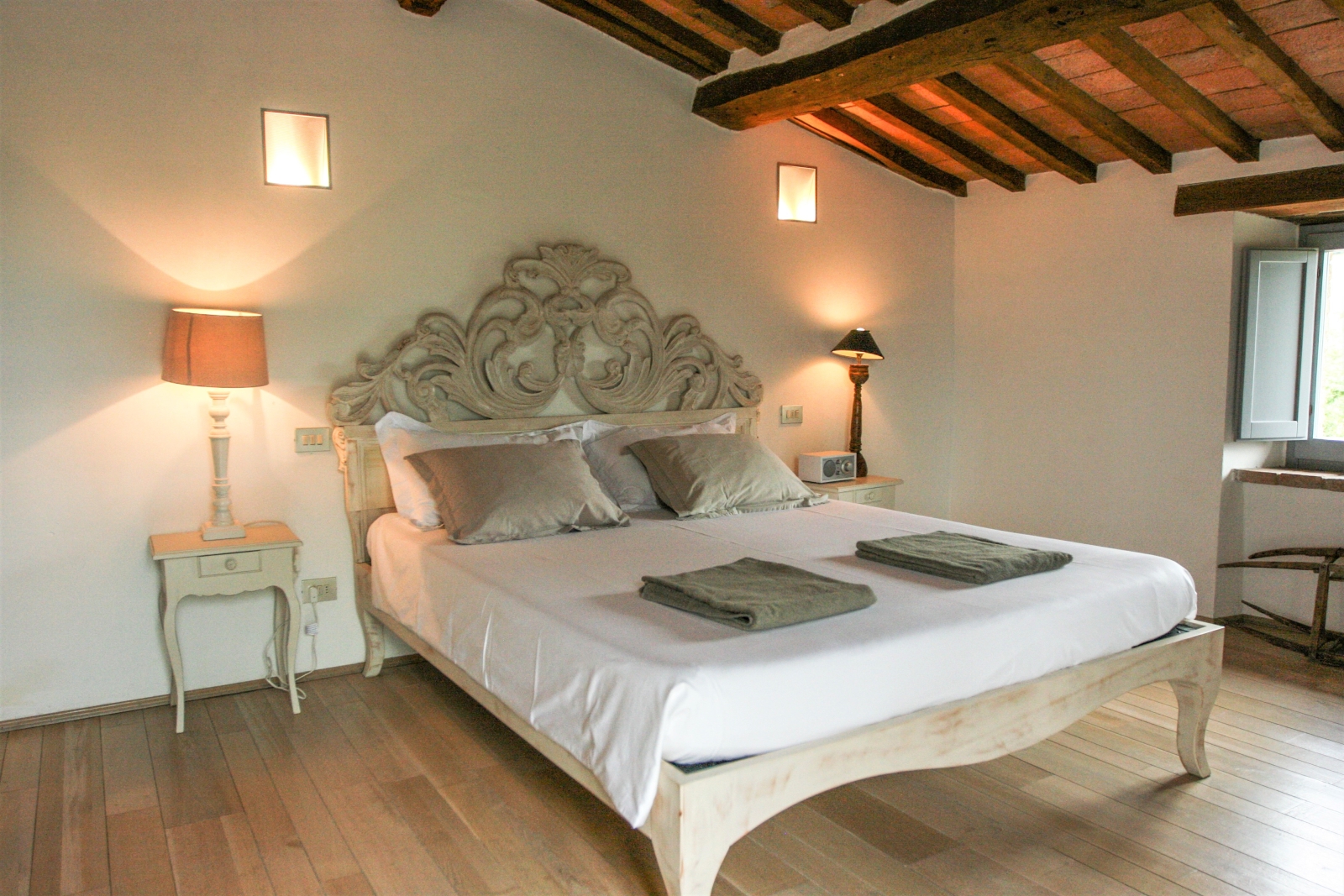 Bedroom with double bed, bedside tables, lamps, radio, windows and ceiling beams at La Spiga in Umbria, Italy