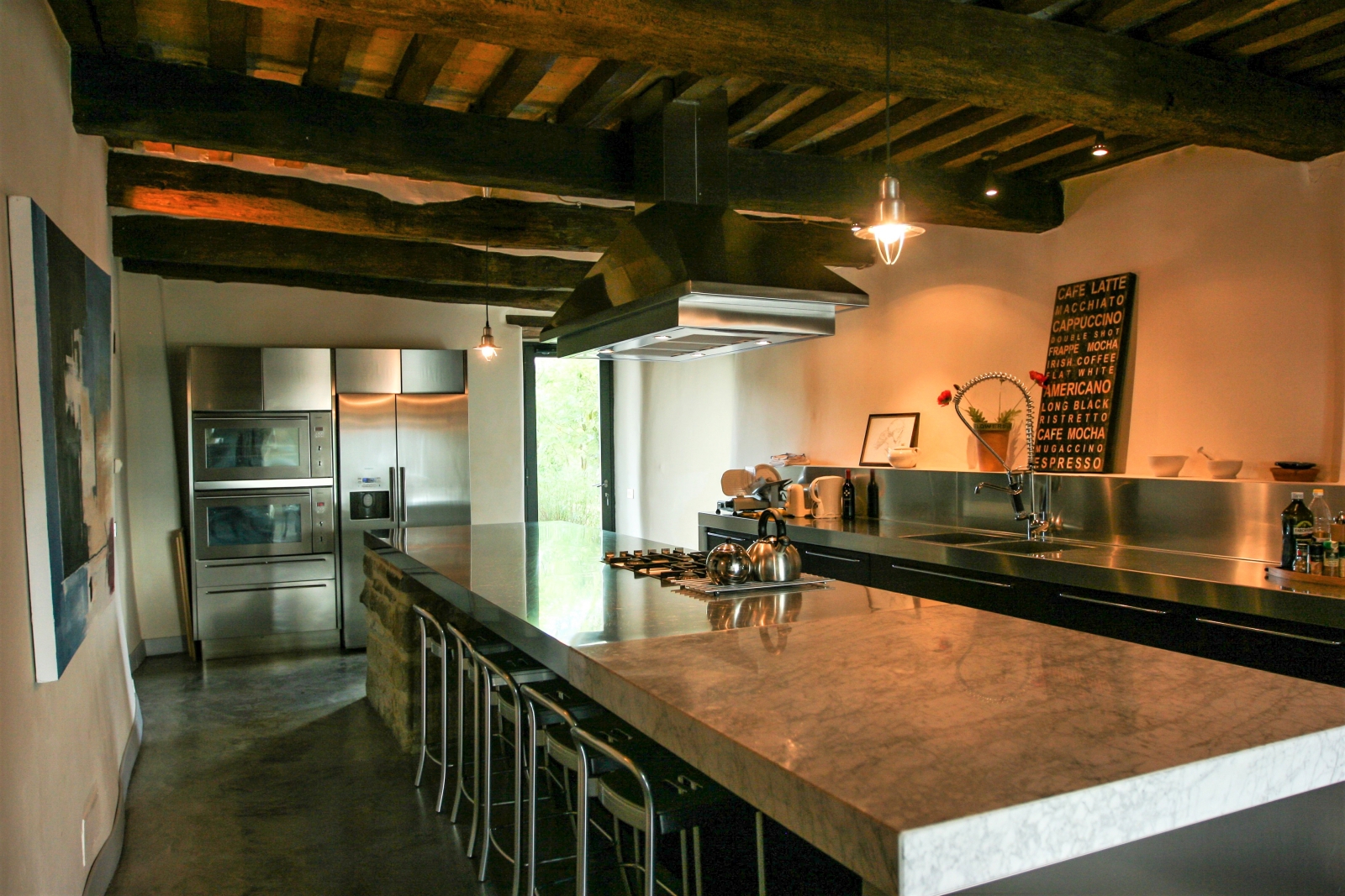 Kitchen with marble island, stools, appliances, artwork, flowers and ceiling beams at La Spiga in Umbria, Italy