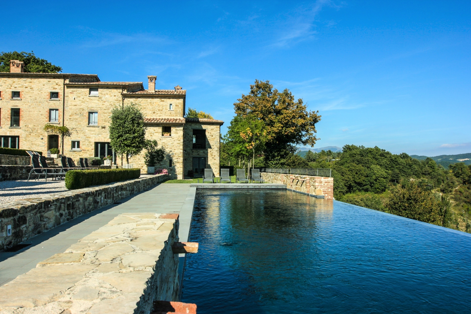 Pool area with countryside view, patio with sun loungers and view of the back of the villa at La Spiga in Umbria, Italy