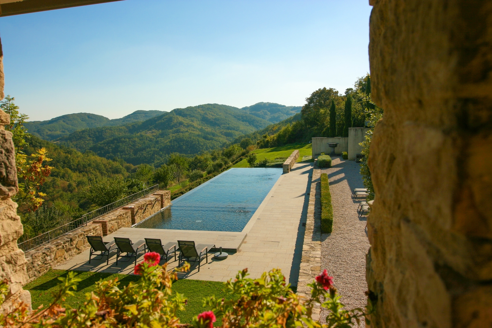 View of pool, sun loungers, flowers and surrounding hills at La Spiga in Umbria, Italy