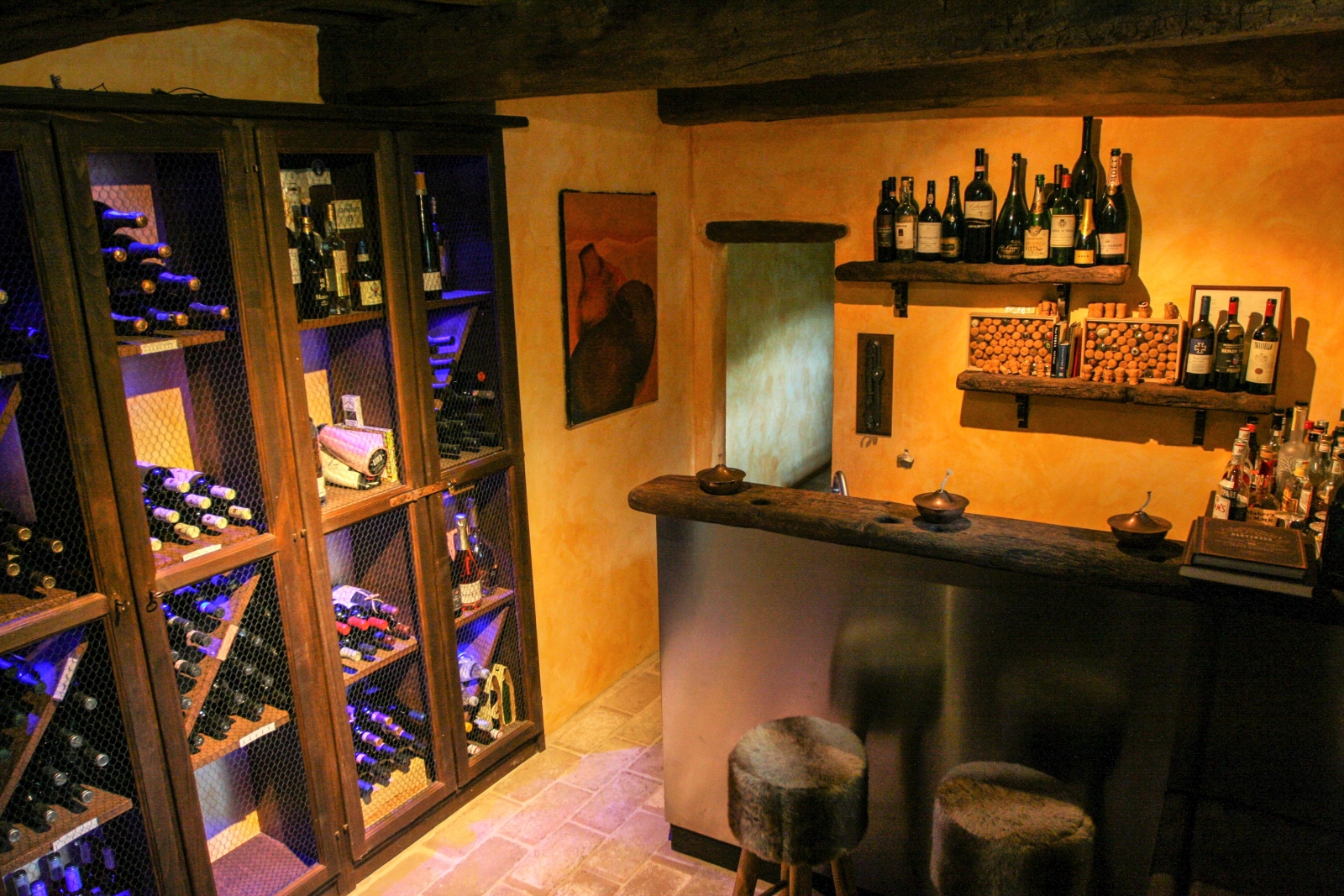 Wine cellar with cabinets, wine bottles, bar area, stools and wooden ceiling beams at La Spiga in Umbria, Italy