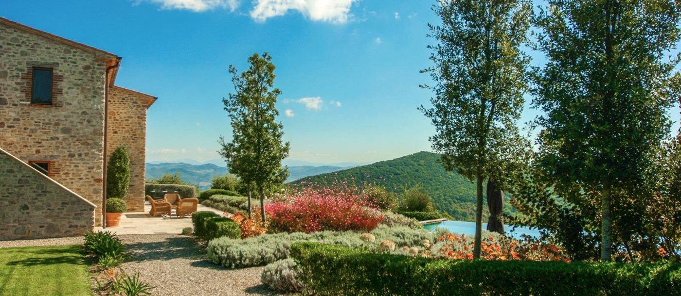 Garden with flowers, trees, hedges, terrace, pool and countryside views at Monticello in Umbria, Italy