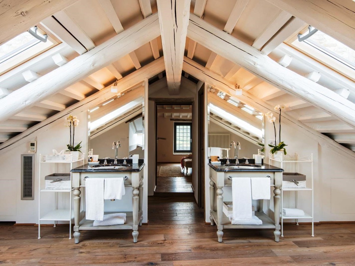 Bathroom with white beamed ceiling and two sinks either side of door leading to bedroom at villa del conte in umbria, Italy
