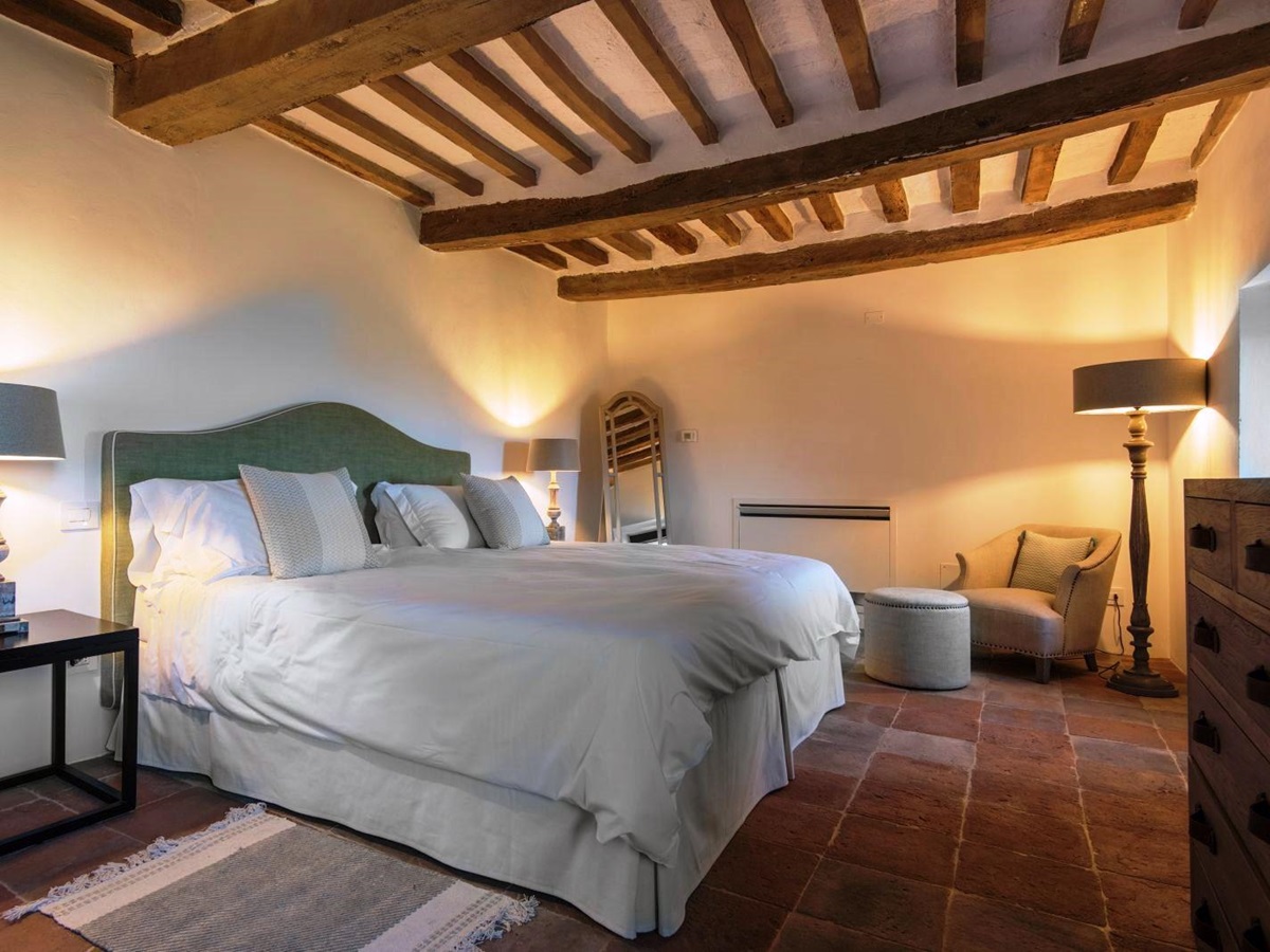 Bedroom with beamed ceiling and double bed with green headboard on terracotta floor at villa del conte in umbria, Italy