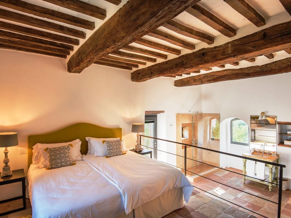 Bedroom with beamed ceiling and double bed with yellow headboard and steps down to bathroom at villa del conte in umbria