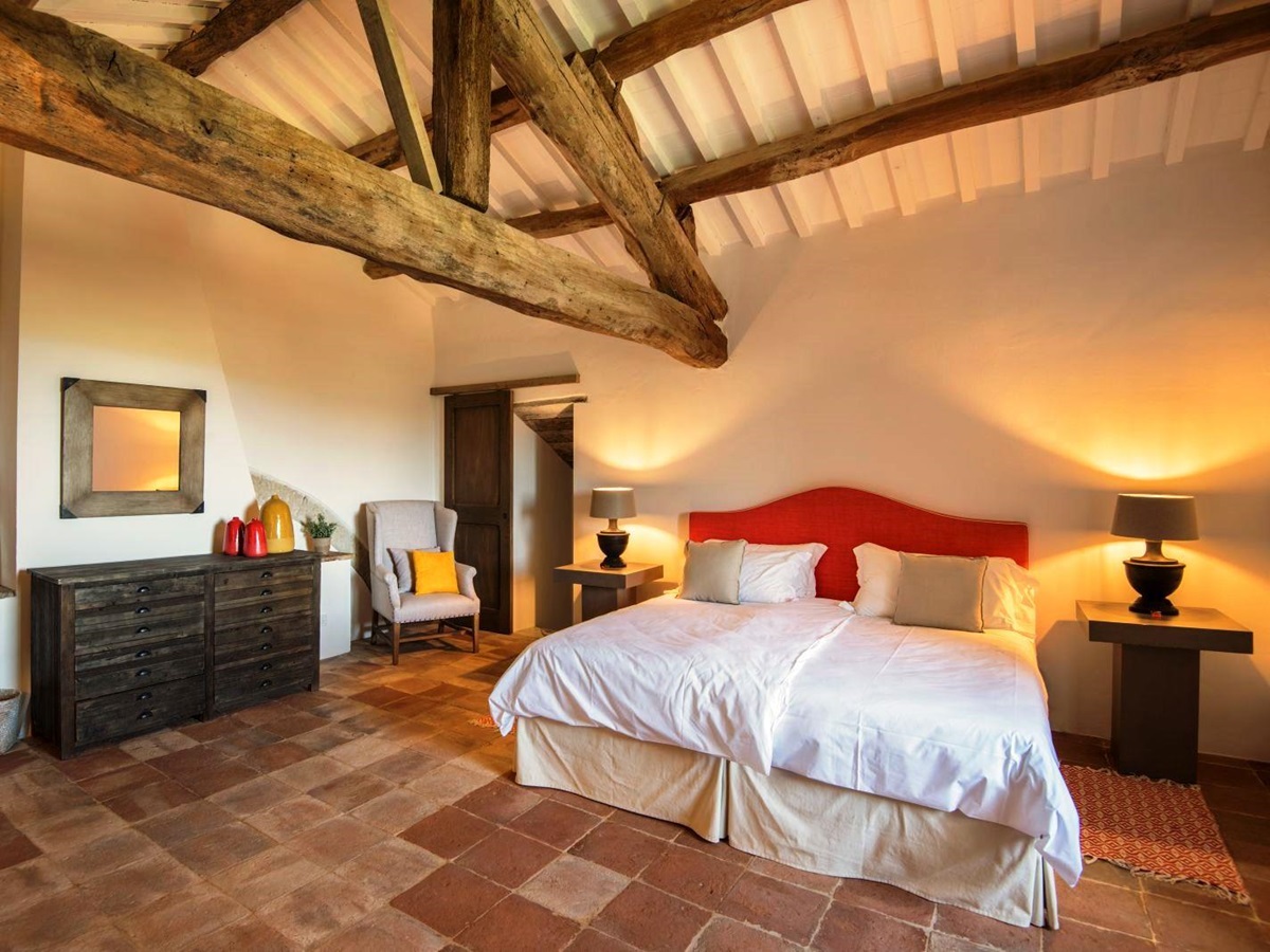 Bedroom with beamed ceiling and double bed with red headboard on terracotta floor at villa del conte in umbria, Italy