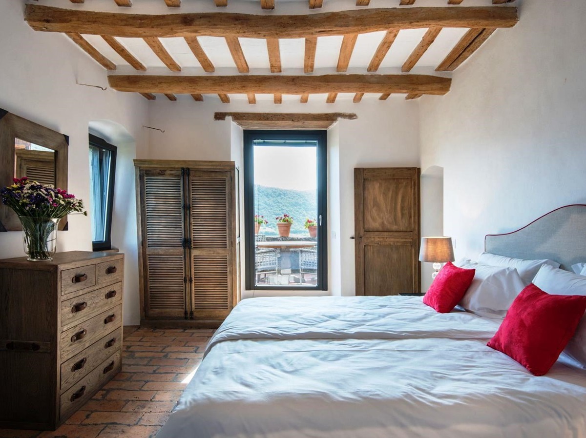 Bedroomwith glass door onto terrace and double bed with red cushions at villa del conte in umbria, Italy