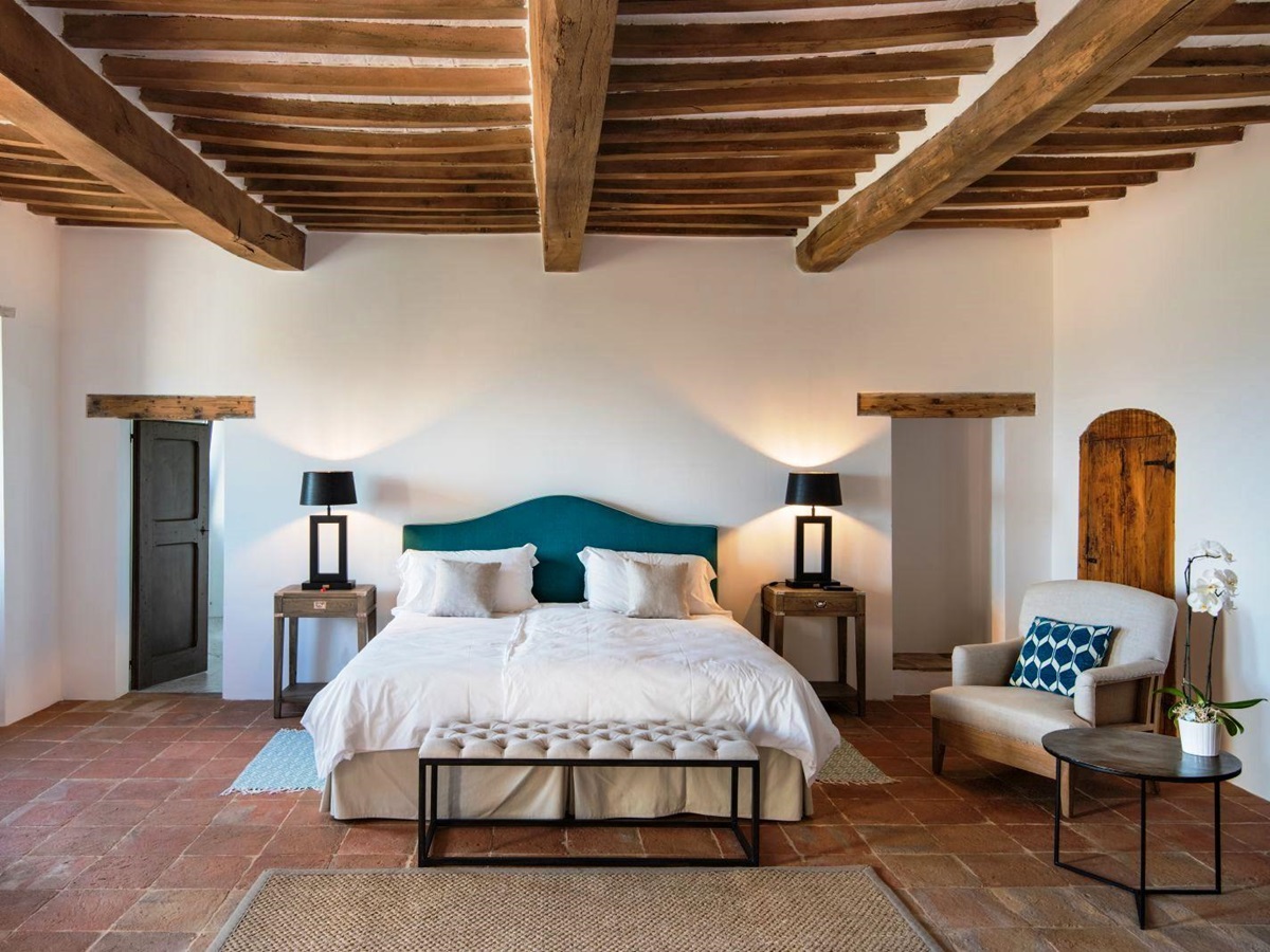 Bedroom with beamed ceiling and double bed with blue headboard on terracotta floor at villa del conte in umbria, Italy