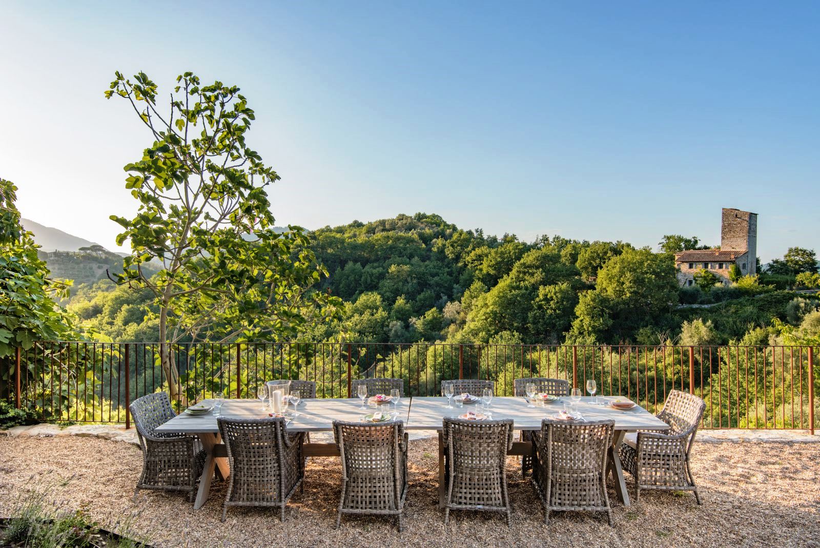outdoor dining area with long wooden table with 10 wicker chairs at villa del conte in umbria, Italy with view of hills