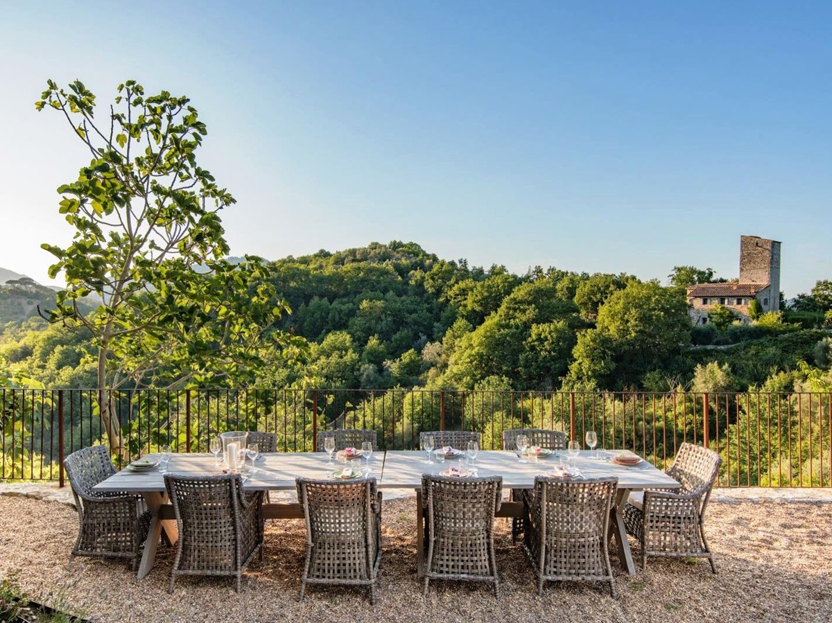 outdoor dining area with long wooden table with 10 wicker chairs at villa del conte in umbria, Italy with view of hills