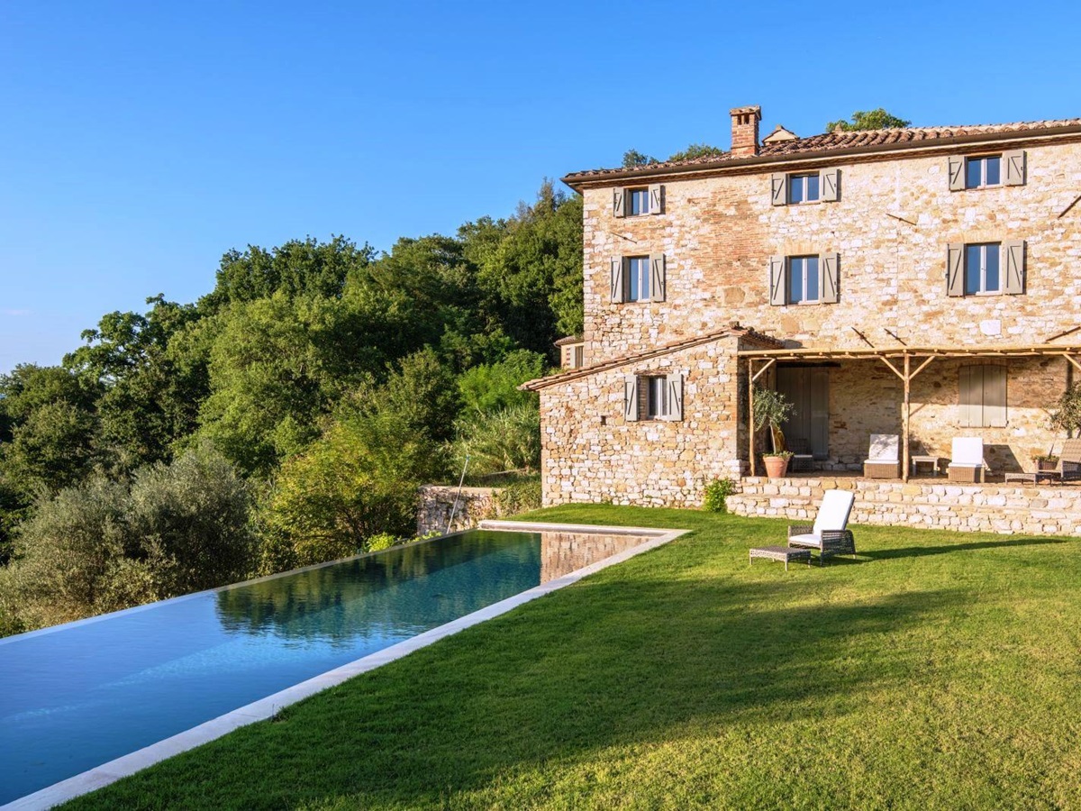 stone house in grounds of villa del conte in umbria, Italy with pool, garden and one chair and table on grass