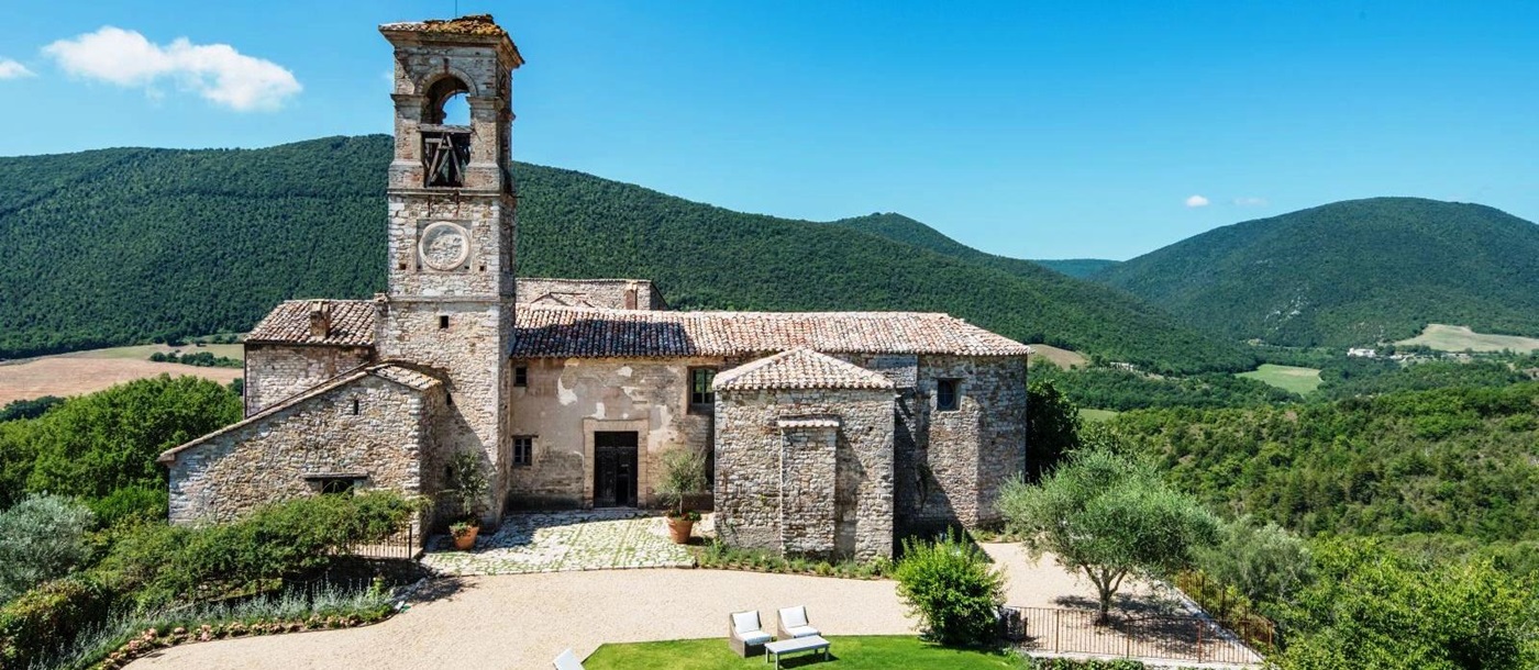 old stone buildings of villa del conte in umbria, Italy with 5 white sunbeds next to pool in front of gravel drive