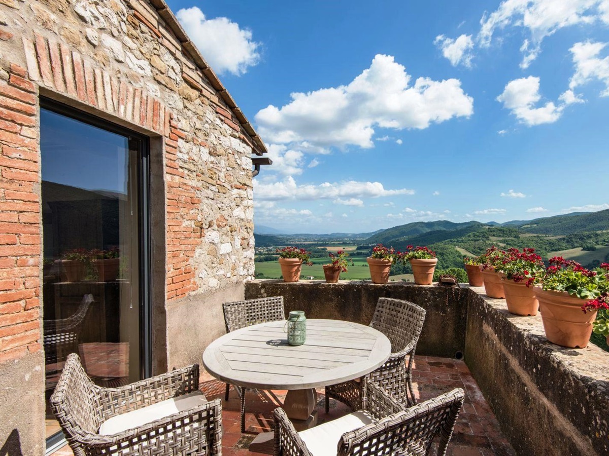 round wooden table with 4 wicker chairs on sun terrace with flowers in pots at villa del conte in umbria, Italy