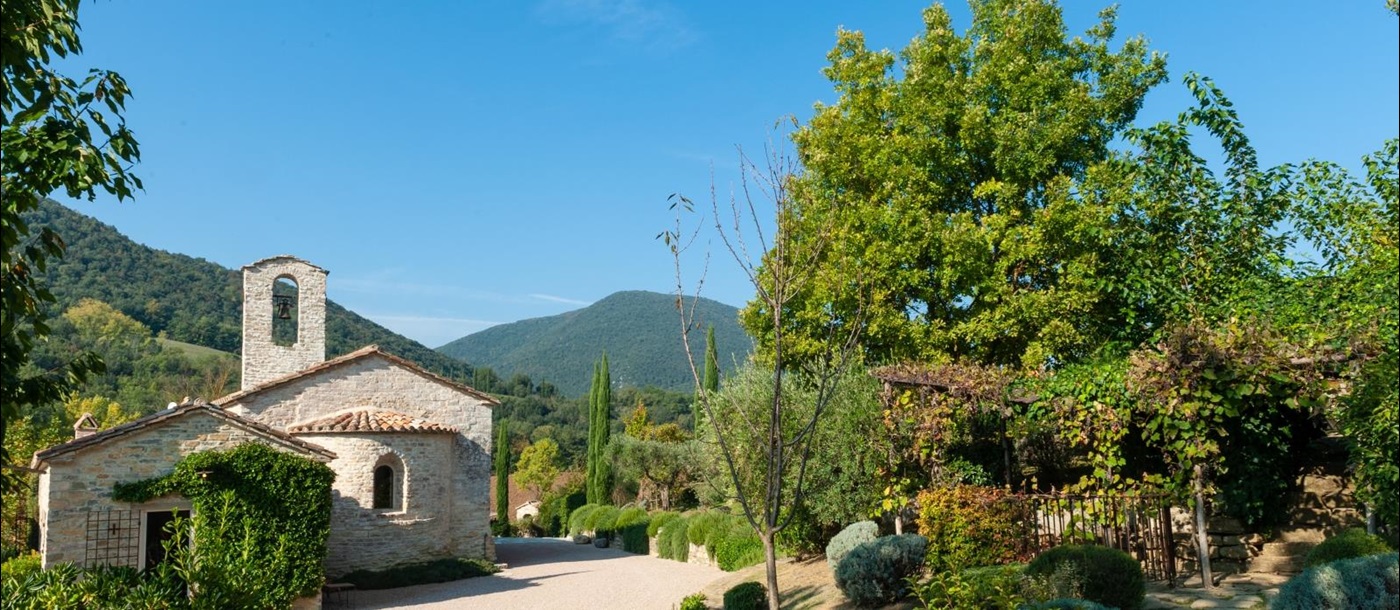 Exterior of villa & garden with pathway, plants, trees and view of surrounding hills at Villa Il Carmine in Umbria, Italy