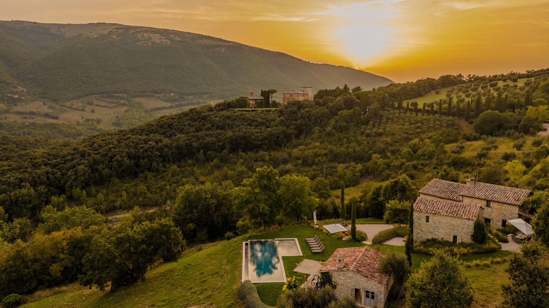 Drone view of Villa Piuma in Umbria with the sun setting featuring the outdoor pool and rolling hills