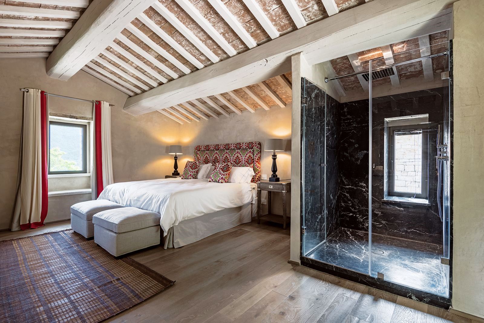Bedroom with king size bed, wooden floors, beamed ceiling, window and large walk in shower at Villa Piuma in Umbria, Italy 