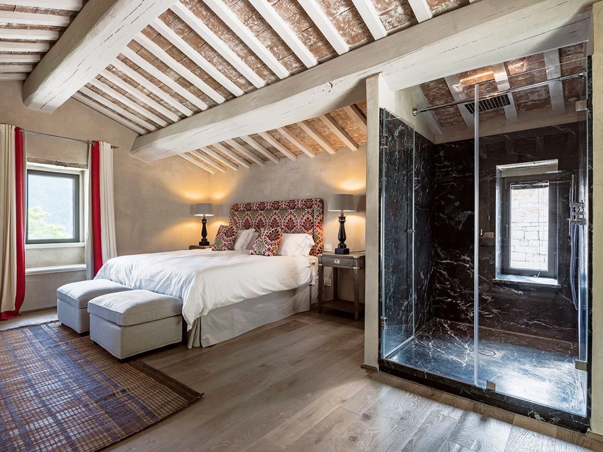 Bedroom with king size bed, wooden floors, beamed ceiling, window and large walk in shower at Villa Piuma in Umbria, Italy