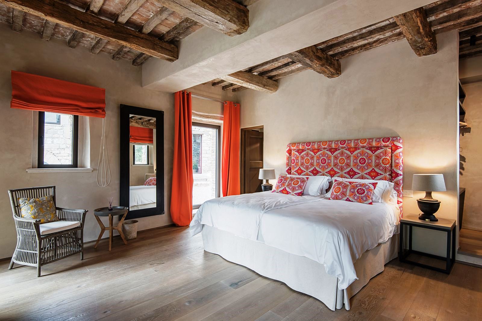 Bedroom with king size bed on wooden floor, orange curtains, chair, table and mirror at Villa Piuma in Umbria, Italy 