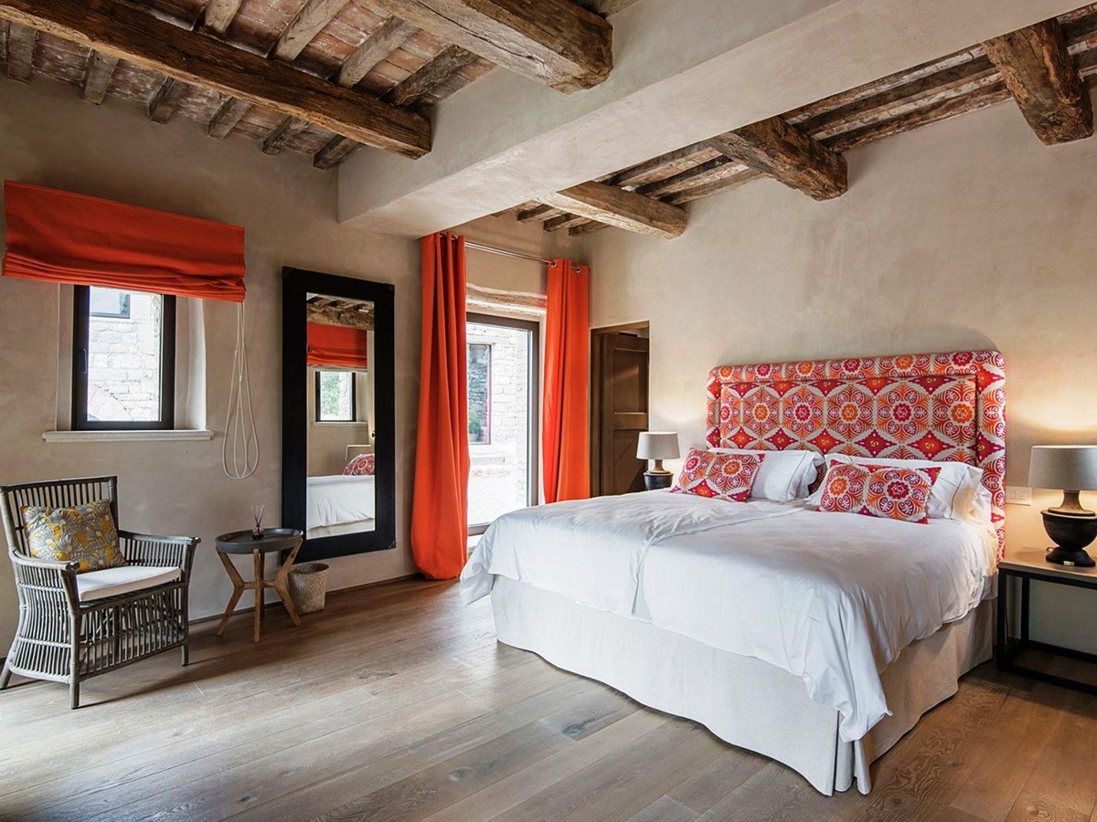 Bedroom with king size bed on wooden floor, orange curtains, chair, table and mirror at Villa Piuma in Umbria, Italy