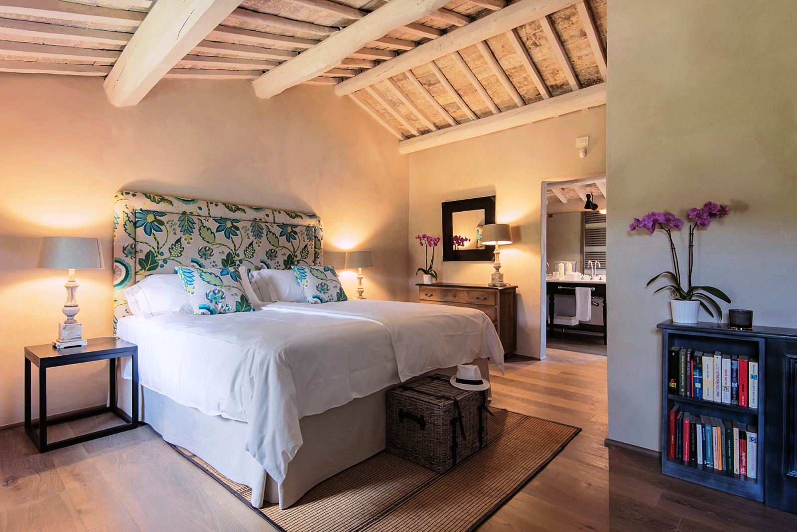 Double bedroom with door to bathroom, wicker basket with panama hat at end of bed at Villa Piuma in Umbria, Italy