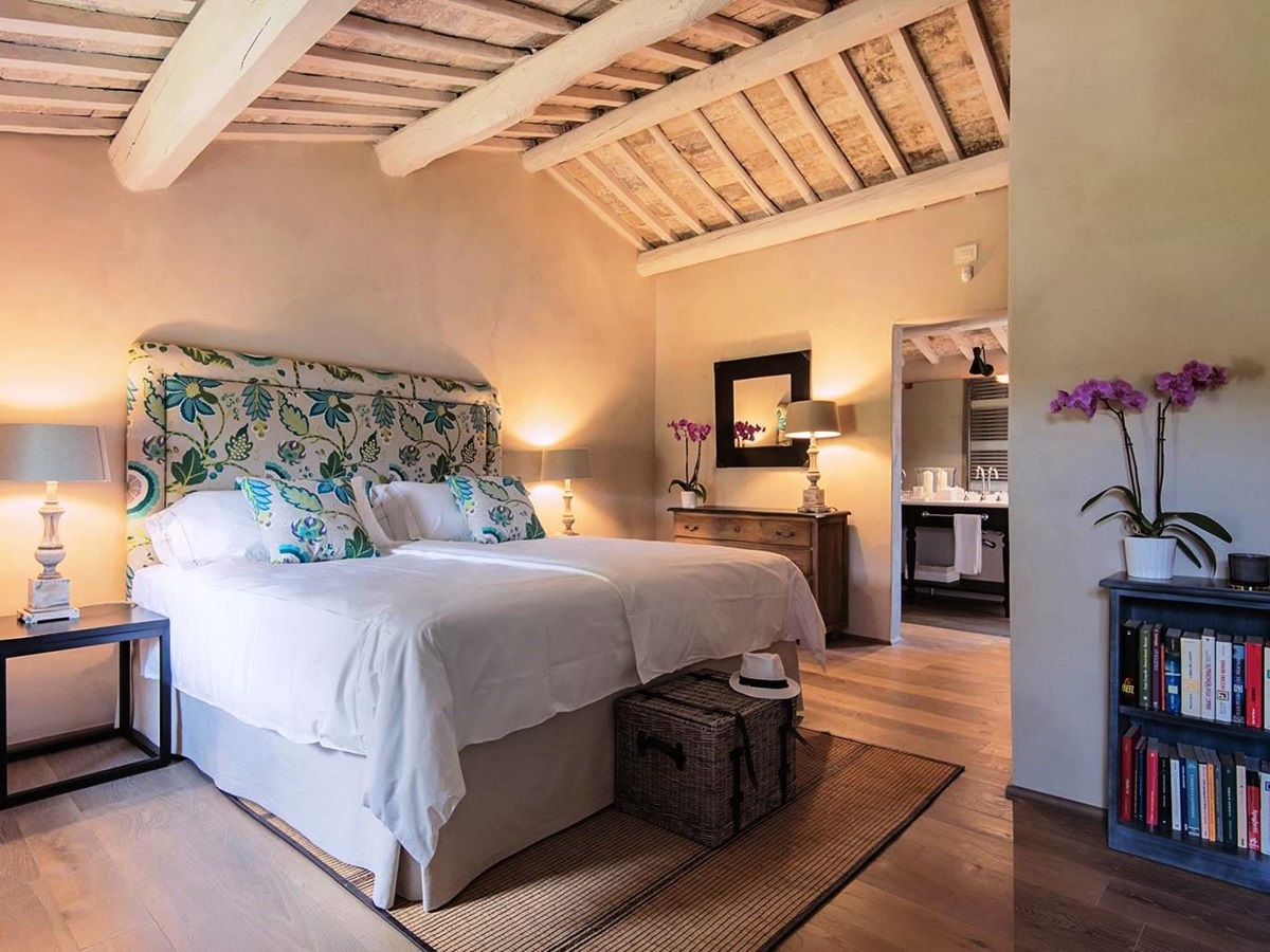 Double bedroom with door to bathroom, wicker basket with panama hat at end of bed at Villa Piuma in Umbria, Italy