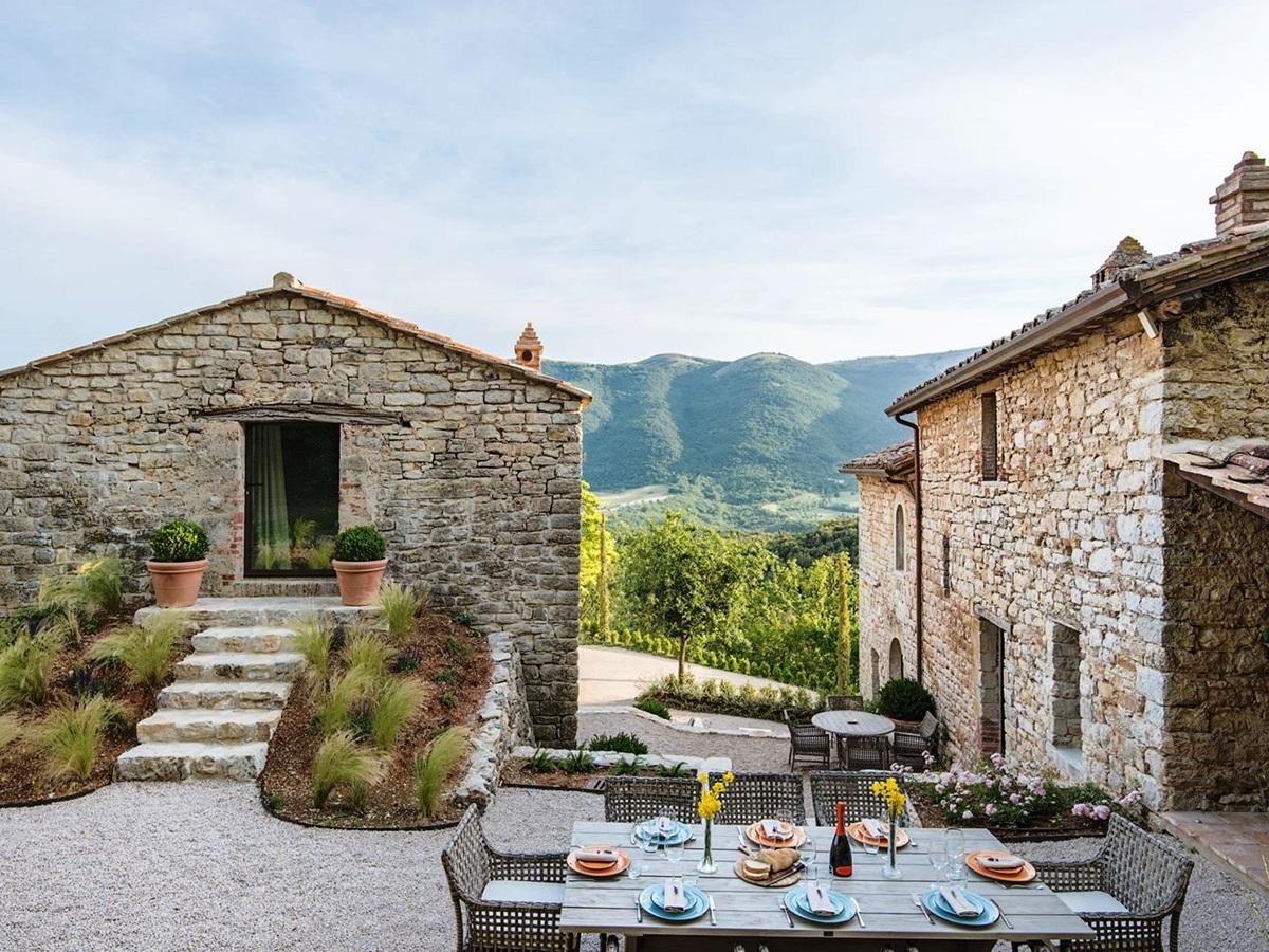 Outdoor dining table with house and annex behind and view of mountains at Villa Piuma in Umbria, Italy
