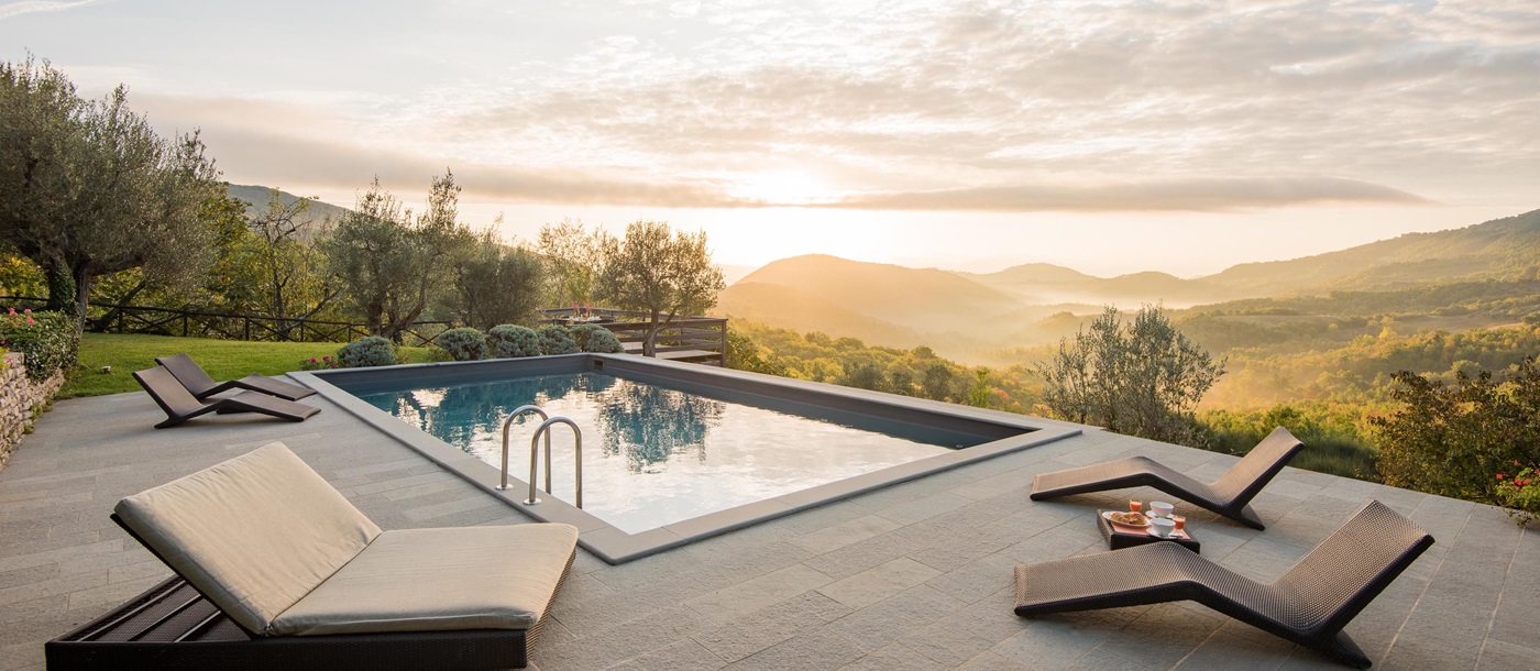 Pool area with patio, sun loungers, food, drink, grass & view of balcony and countryside at Villa Pizzicato in Umbria, Italy