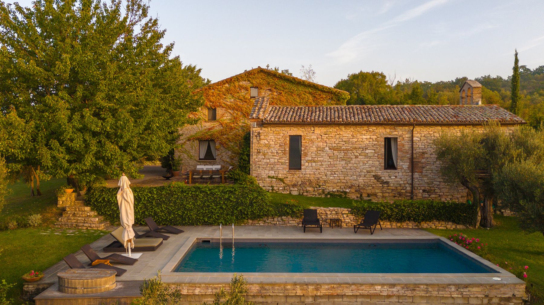 Pool area at Villa Pizzicato in Umbria featuring black sunbeds and a white umbrella with the villa behind