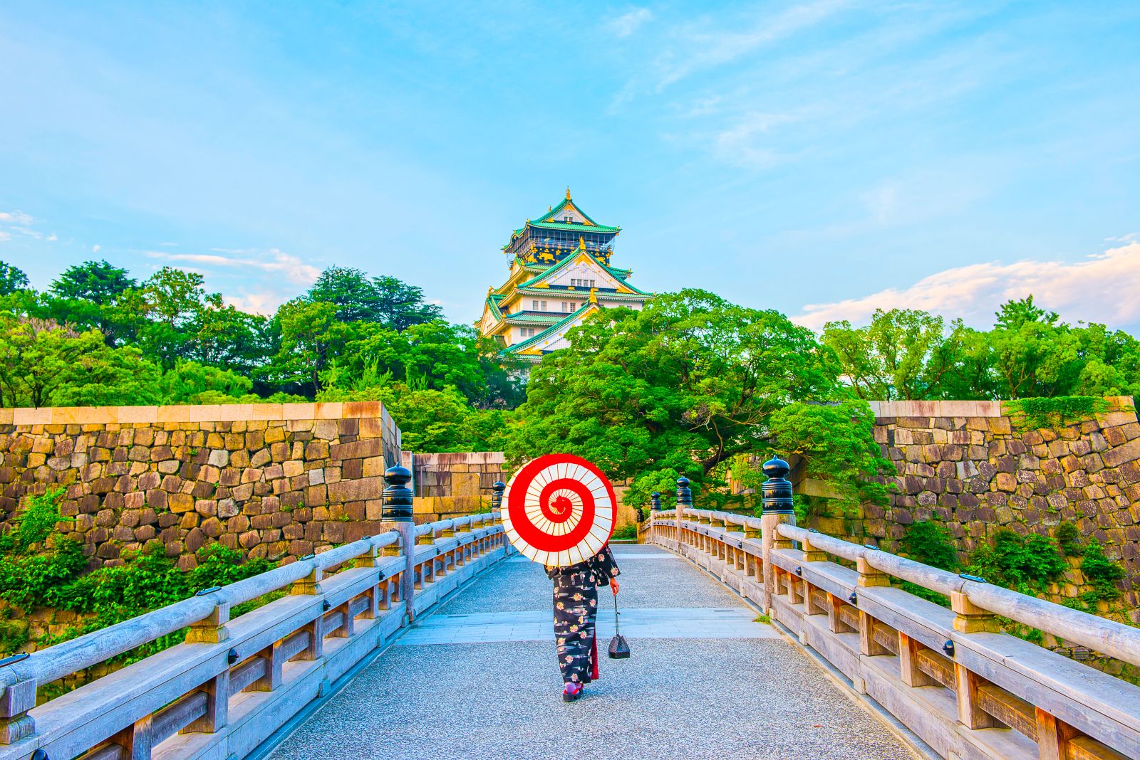 Lady with parasol strolling through Osaka park towards the castle